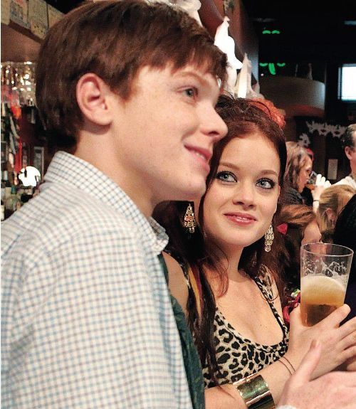 two people standing next to each other at a bar with drinks in front of them