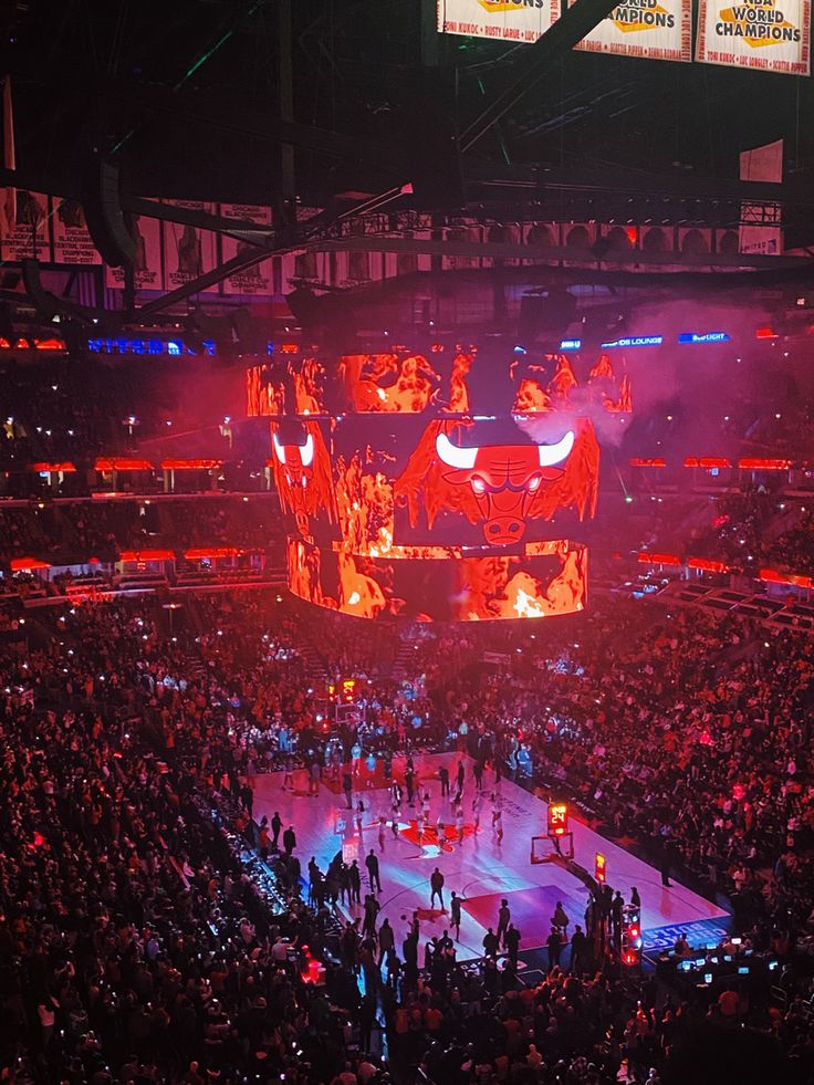 an arena filled with lots of people standing on top of a basketball court at night