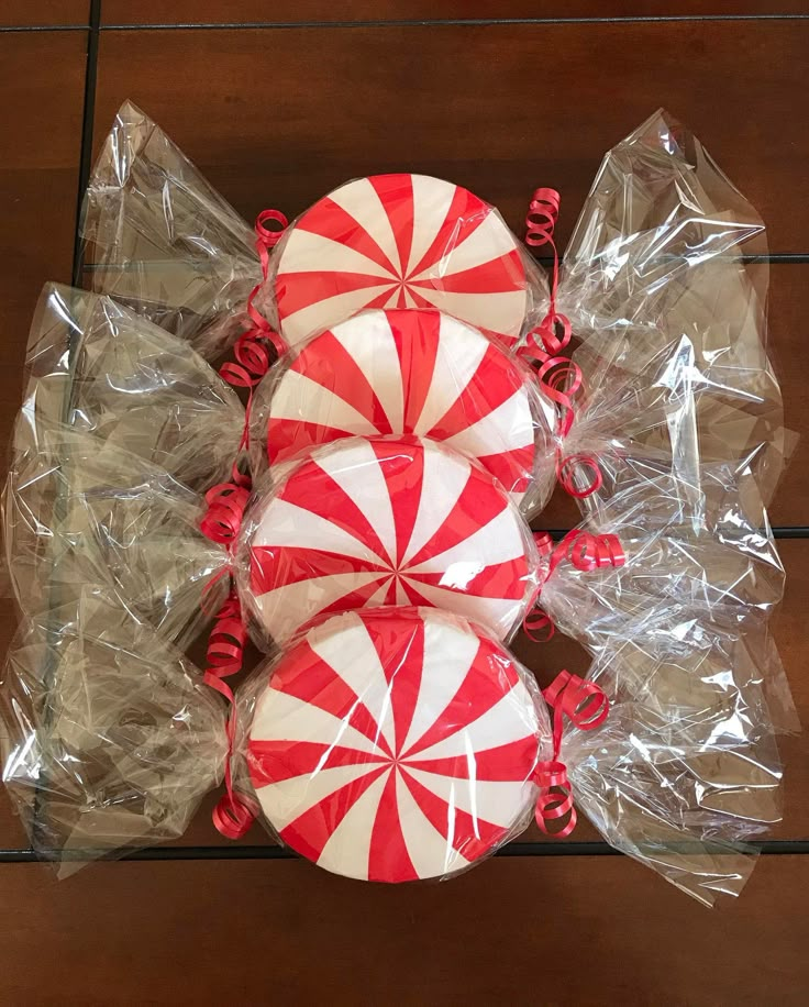 three red and white lollipops wrapped in plastic on top of a wooden table