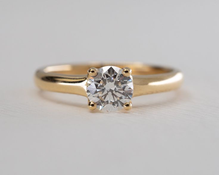 a yellow gold engagement ring with a round diamond in the center, on a white surface