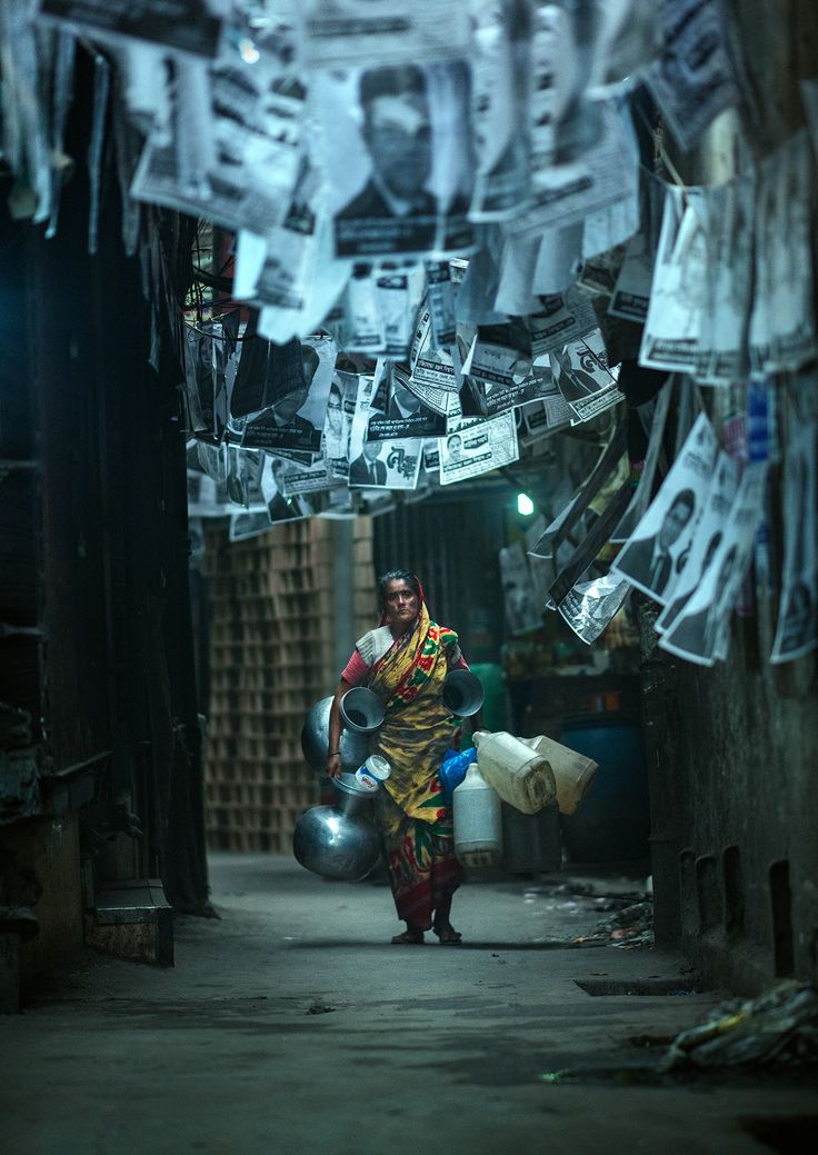 a woman walking down a narrow alley way with papers hanging from the ceiling above her