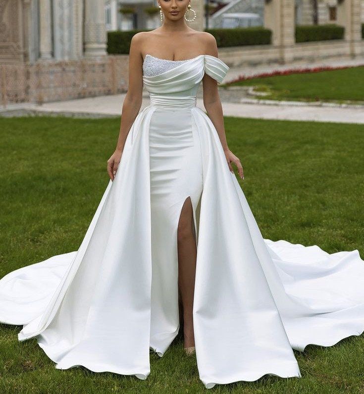 a woman in a white wedding dress standing on the grass with her legs slited