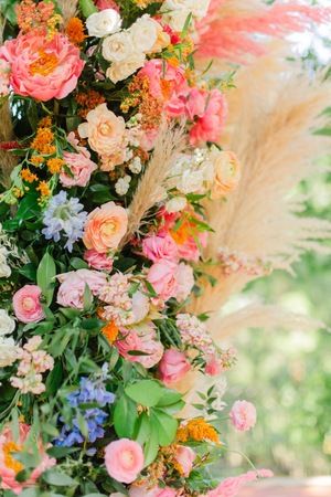 an arrangement of flowers and grasses on a table in front of some trees with long grass