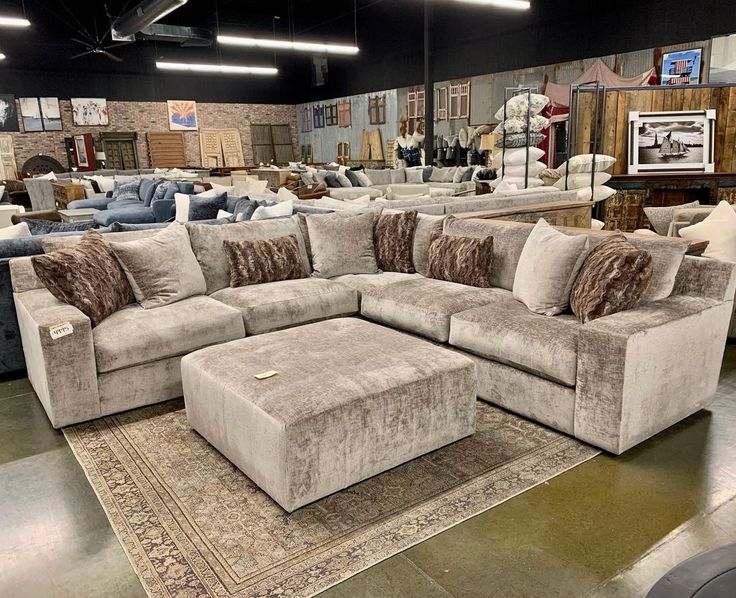 a couch and ottoman in a large room with lots of furniture on the floor for sale