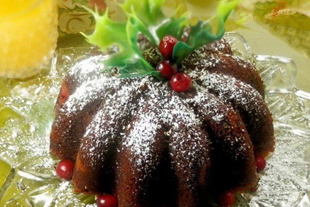 a bundt cake covered in powdered sugar and topped with holly berries on a glass platter