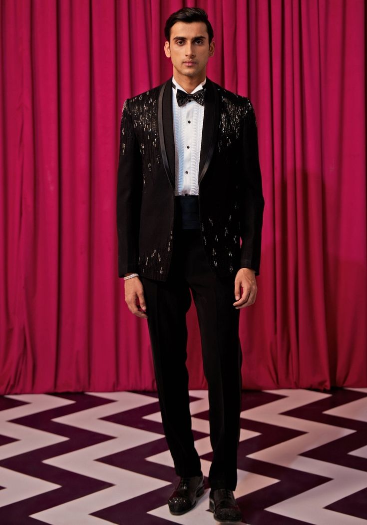 Step into elegance with our Black Textured Tuxedo Set. Crafted from luxurious textured suiting, this set features an elegant black blazer embellished with intricate linear embroidery. Paired with an embellished bowtie, sash, pintuck shirt, and pants, it's the ideal choice for cocktails or wedding receptions. Make a statement and exude sophistication in this stunning tuxedo set. Components : 5 (Blazer, Shirt, Bowtie, Sash and Pants) Composition : Textured Suiting Care: Dry Clean Only and Vacuum Storage This product can be customized for sleeves, length of blouse and neckline Delivery : 4-6 weeks as the product is hand crafted. Check Size Guide or choose MySize for free customisation (All Sizes above XL can be made at 15% additional cost) For more information and sizes please contact fabilic Embellished Notch Lapel Suits For Semi-formal Occasions, Tailored Party Wear Blazer For Semi-formal Occasions, Designer Evening Suits For Festive Occasions, Designer Festive Evening Suits, Tailored Evening Party Wear Suits, Elegant Tuxedo For Black-tie Festive Events, Elegant Tuxedo For Festive Party, Elegant Tuxedo For Gala And Festive Occasions, Festive Tailored Blazer For Evening