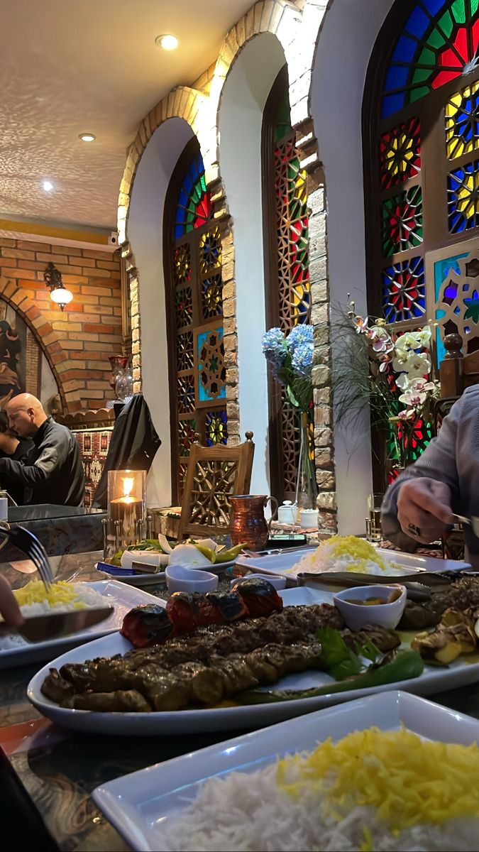 people are sitting at a table with plates of food in front of stained glass windows