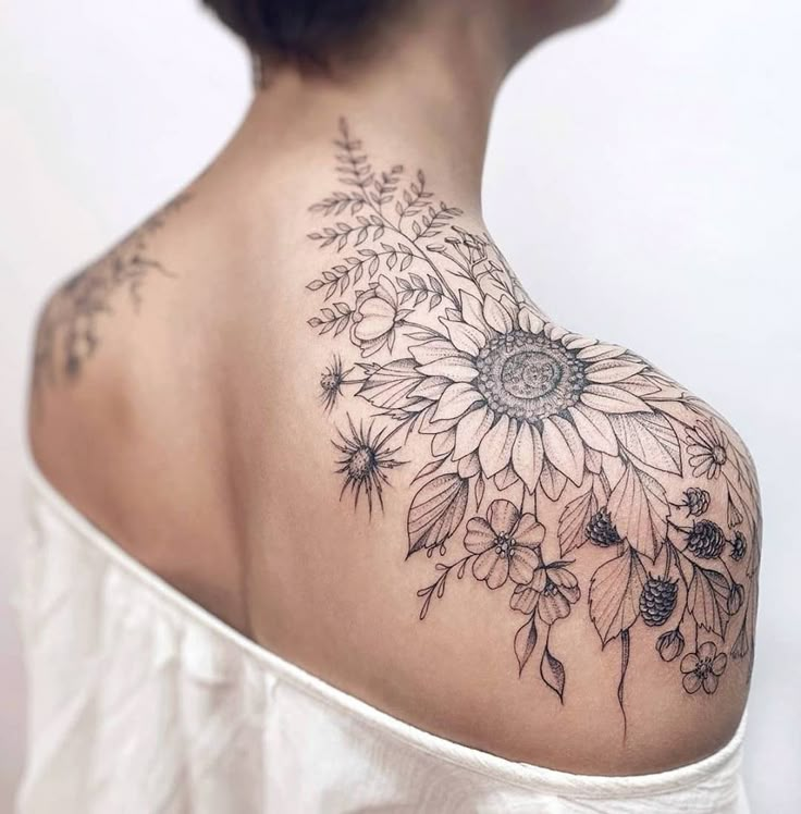 the back of a woman's shoulder with sunflowers and leaves on it