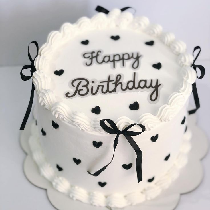 a white cake with black hearts and the words happy birthday written on it is sitting on a plate