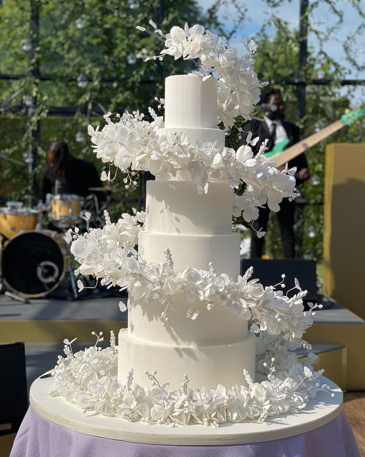 a wedding cake with white flowers on top is sitting on a table in front of a stage