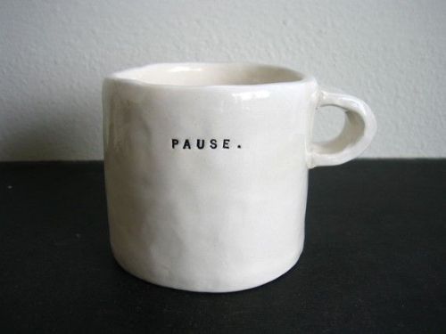 a white coffee cup with the word pause written in black on it sitting on a table