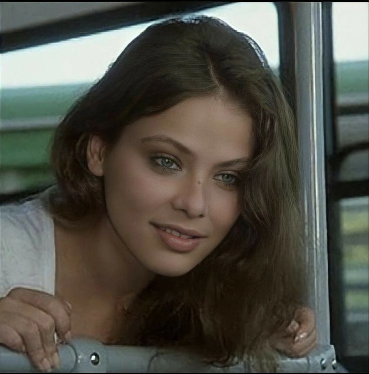 a woman with long hair sitting in a car looking at the camera while holding her hand on her shoulder