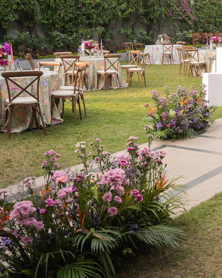 tables and chairs set up in the middle of a lawn with flowers on them, surrounded by greenery