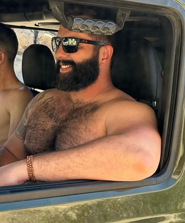 two men sitting in the back seat of a vehicle with no shirts on, one man is wearing sunglasses