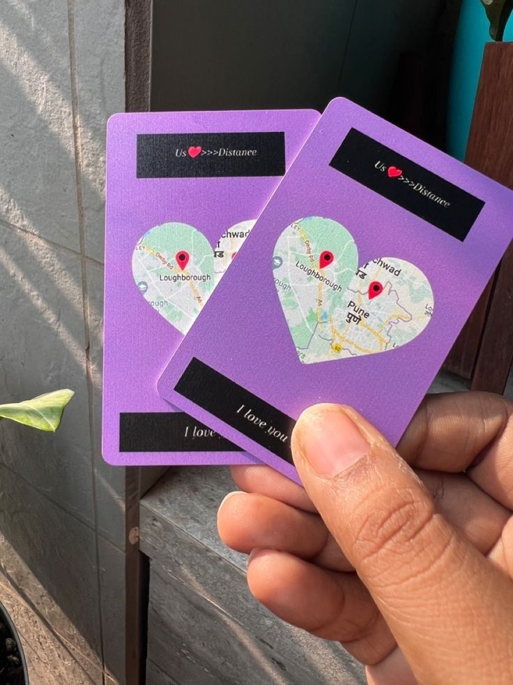 two purple cards with hearts on them are held in someone's hand near a potted plant