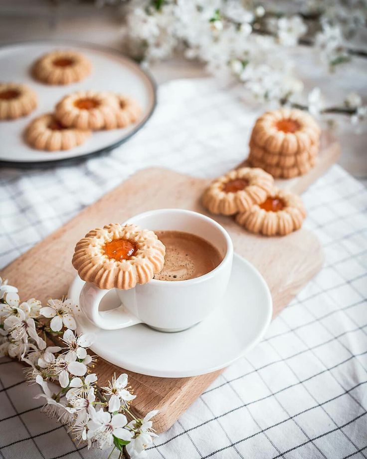 there is a cup of coffee and some cookies on the table next to it with flowers