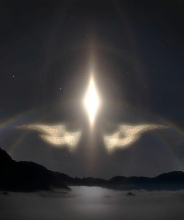 two angel wings are in the sky with a bright halo above them and mountains below