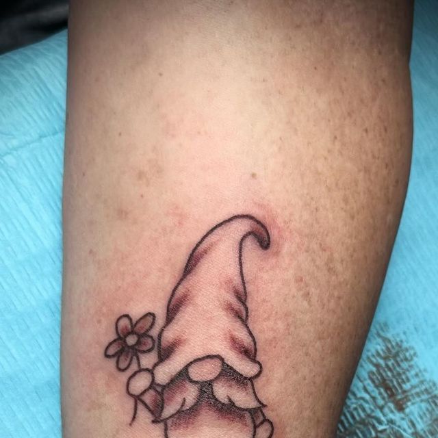 a small gnome's hat with flowers on the side of his leg tattoo design