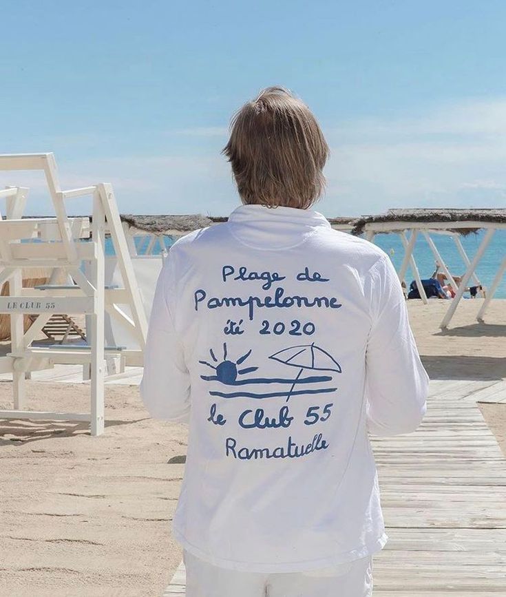 the back of a person wearing white clothing on a pier next to the ocean and water