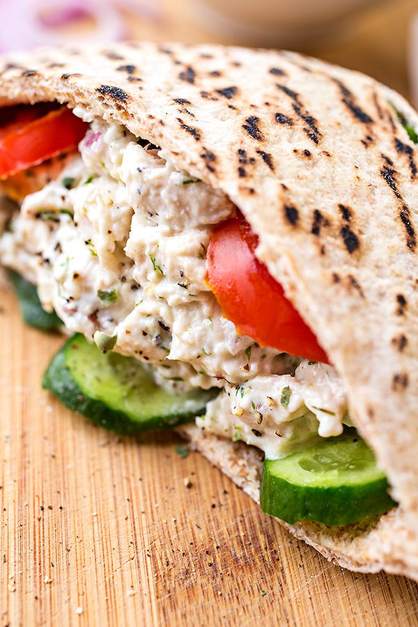 a close up of a chicken salad sandwich on a cutting board with tomatoes and cucumbers