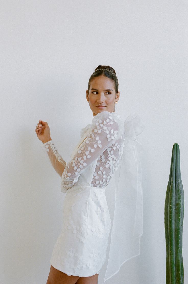 a woman standing next to a cactus wearing a white dress and holding her fist up