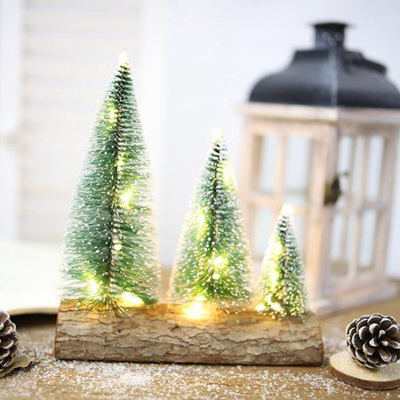 small christmas trees are lit up on a wooden block with pine cones in the foreground