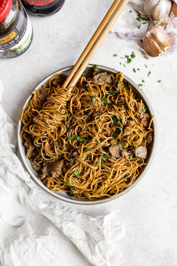 a bowl filled with noodles and meat next to two chopsticks on the side