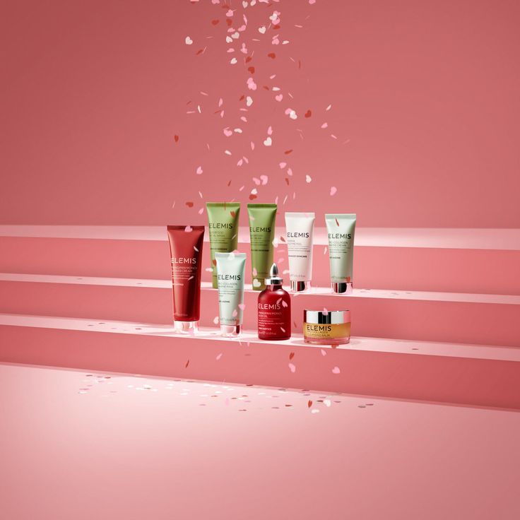 an assortment of skin care products are displayed on a pink background with confetti falling from the top