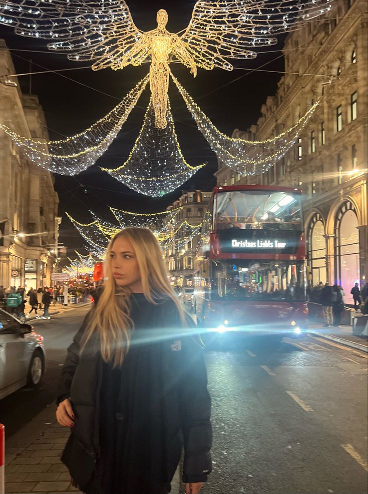 a woman standing in front of a double decker bus on a city street at night