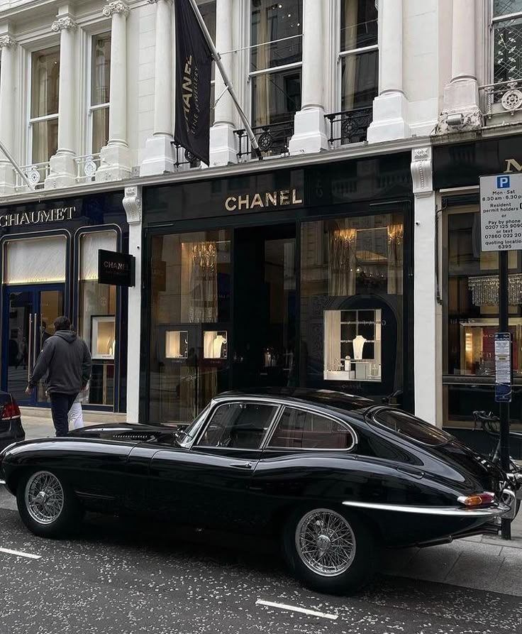 an old black car parked on the side of the road in front of a chanel store