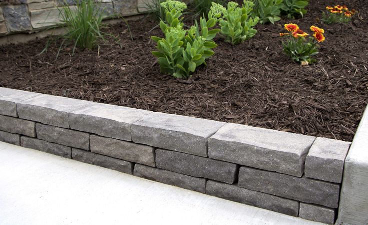 a garden with flowers and plants growing in the ground next to a stone wall that has been made out of concrete blocks