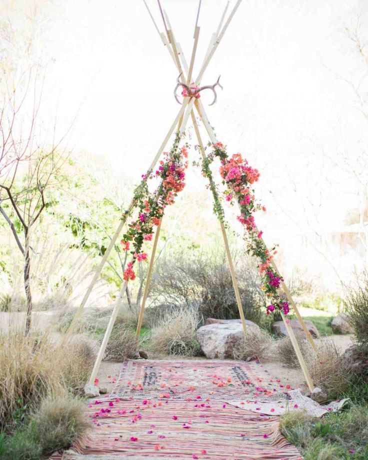 a teepee with pink flowers on it in the middle of some grass and bushes