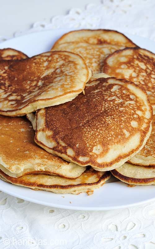 a white plate topped with pancakes on top of a lace doily covered table cloth