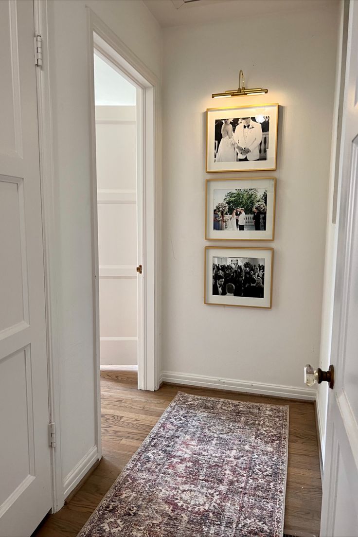 a hallway with pictures on the wall and a rug in front of an open door