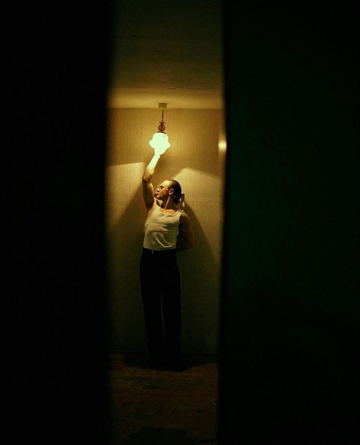 a woman standing in a dark room holding a light bulb above her head and looking at the camera