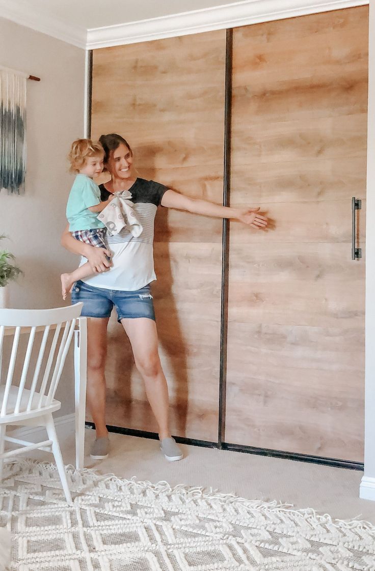 a woman holding a child standing in front of a sliding door with wood paneling