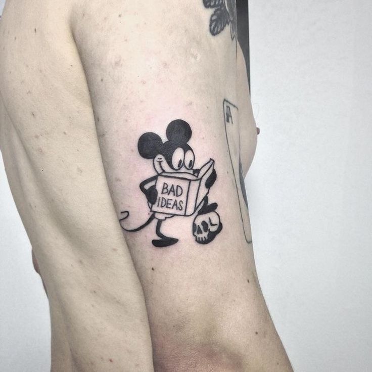 a man with a tattoo on his arm that says bad ideas and mickey mouse reading a book