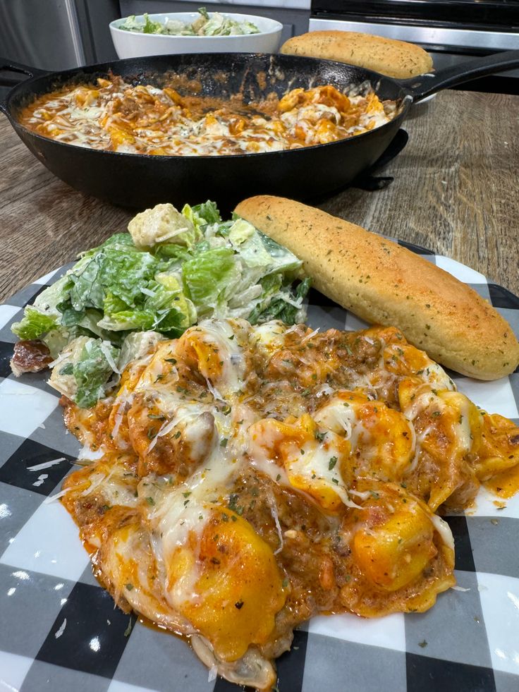 some food is sitting on a checkered table cloth and next to a skillet