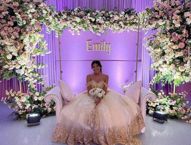 a woman in a wedding dress sitting on a chair with flowers around her and the backdrop behind her