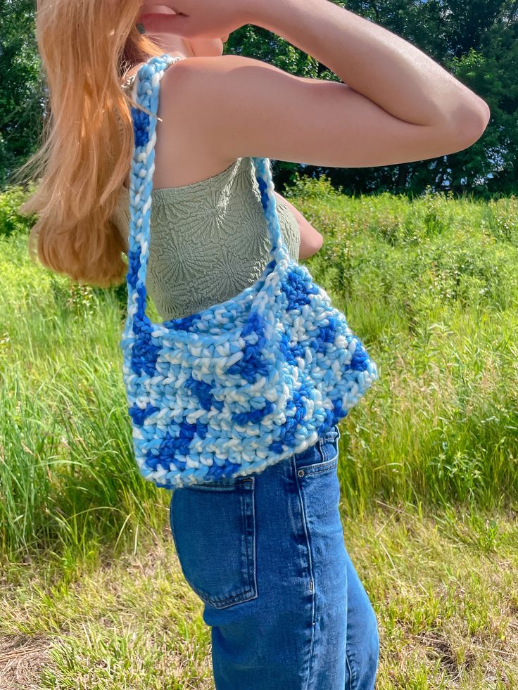 a woman wearing a blue crocheted bag in the grass with her hand on her shoulder