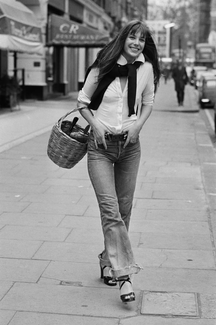 a woman walking down the street with a basket in her hand and smiling at the camera