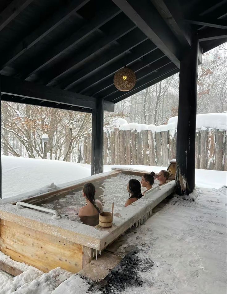 three people sitting in an outdoor hot tub with snow on the ground