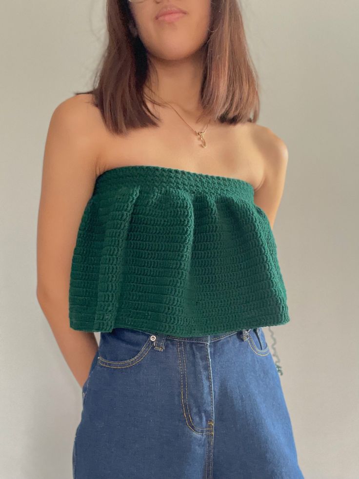 a woman wearing glasses and a green top is standing in front of a white wall