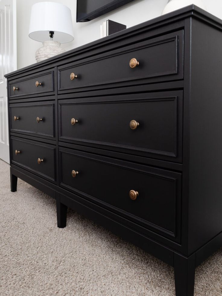 a black dresser with gold knobs in a white room next to a large mirror