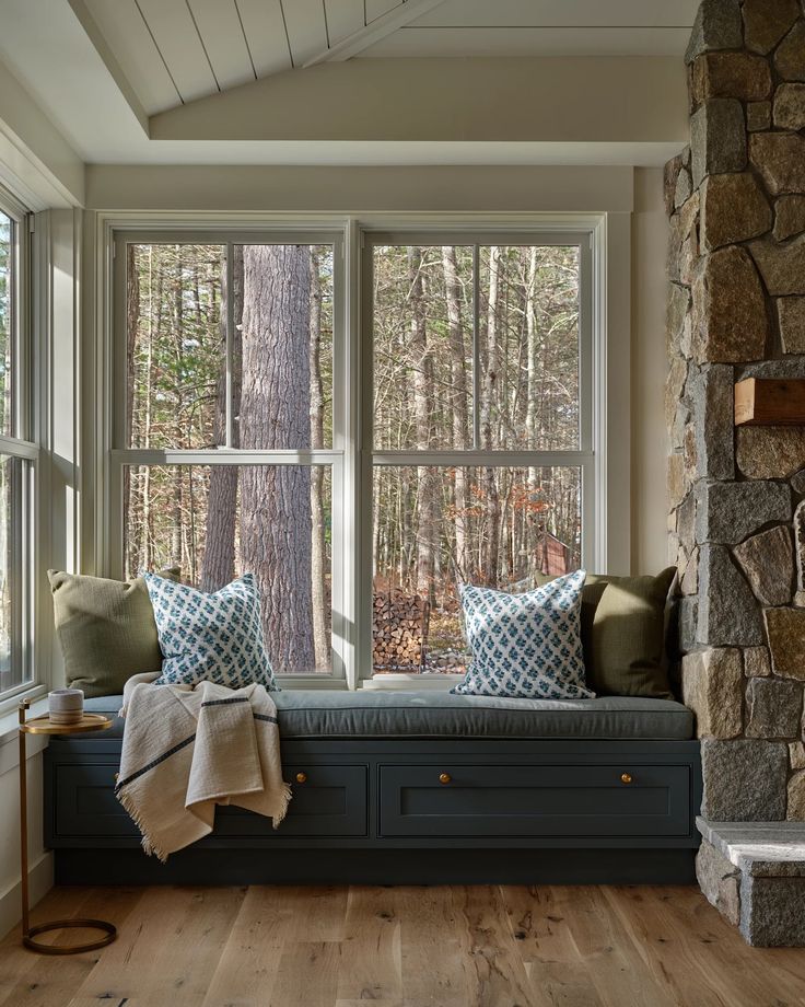 a window seat with pillows and blankets on it in front of a stone fireplace mantel