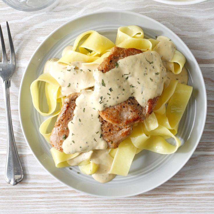 a white plate topped with meat covered in gravy next to a fork and knife