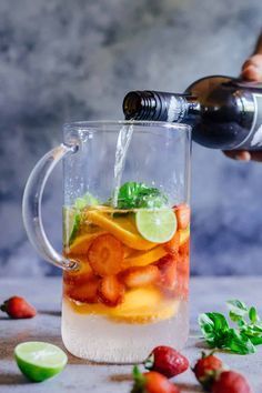 someone pouring water into a pitcher filled with fruit