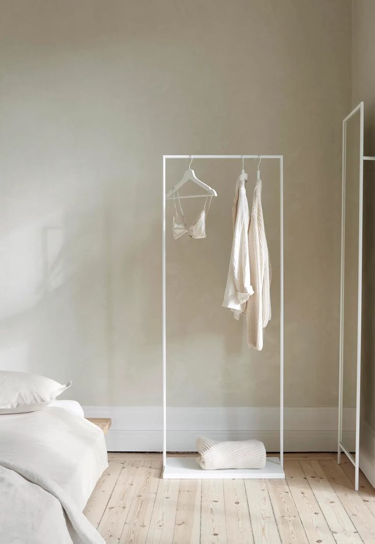 an empty bedroom with clothes hanging on the rack and bed in the foreground next to it