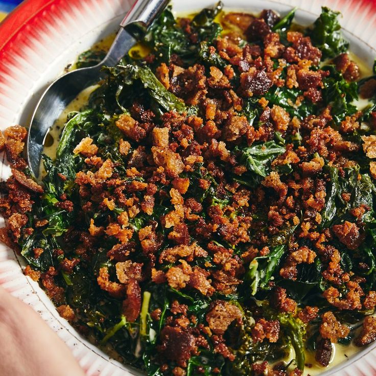 a bowl filled with meat and greens on top of a red and white paper plate