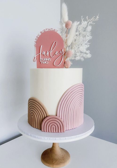 there is a pink and white cake on the table with feathers around it that says happy birthday